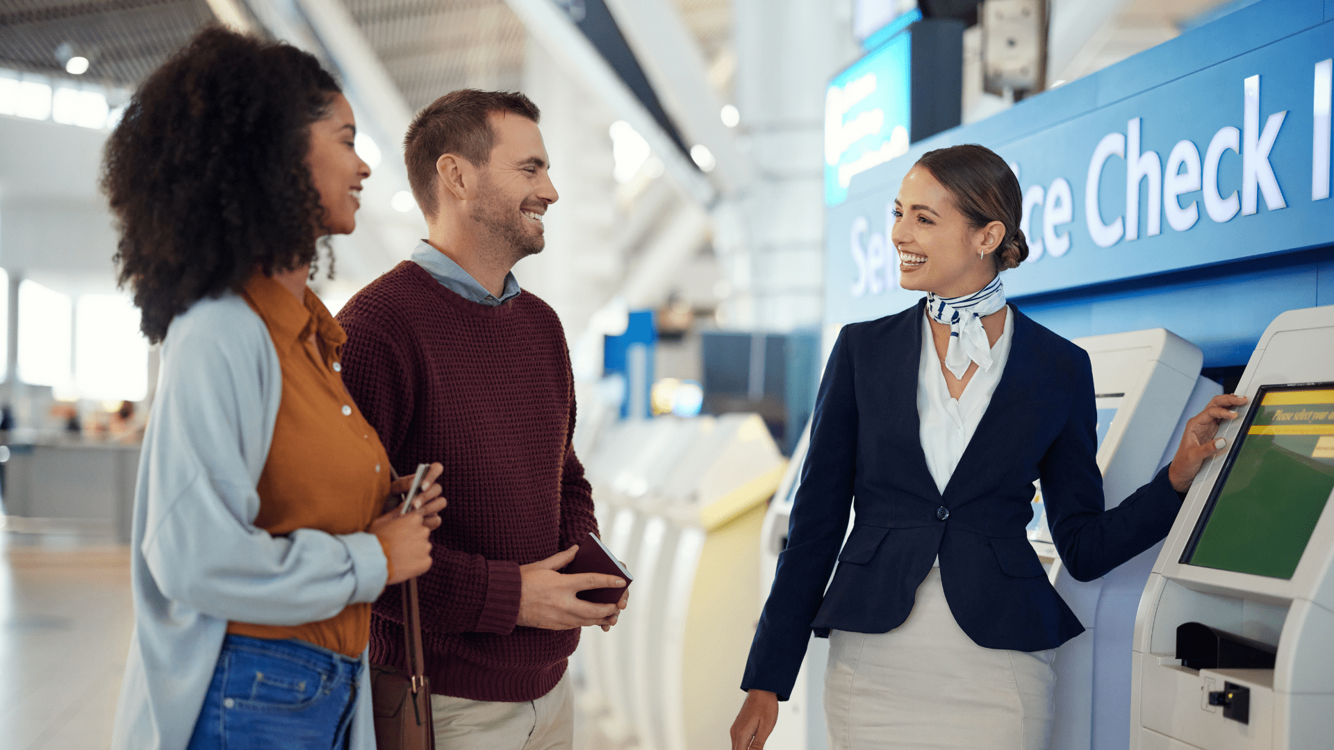 An airport employee assists two passengers with self-service check-in